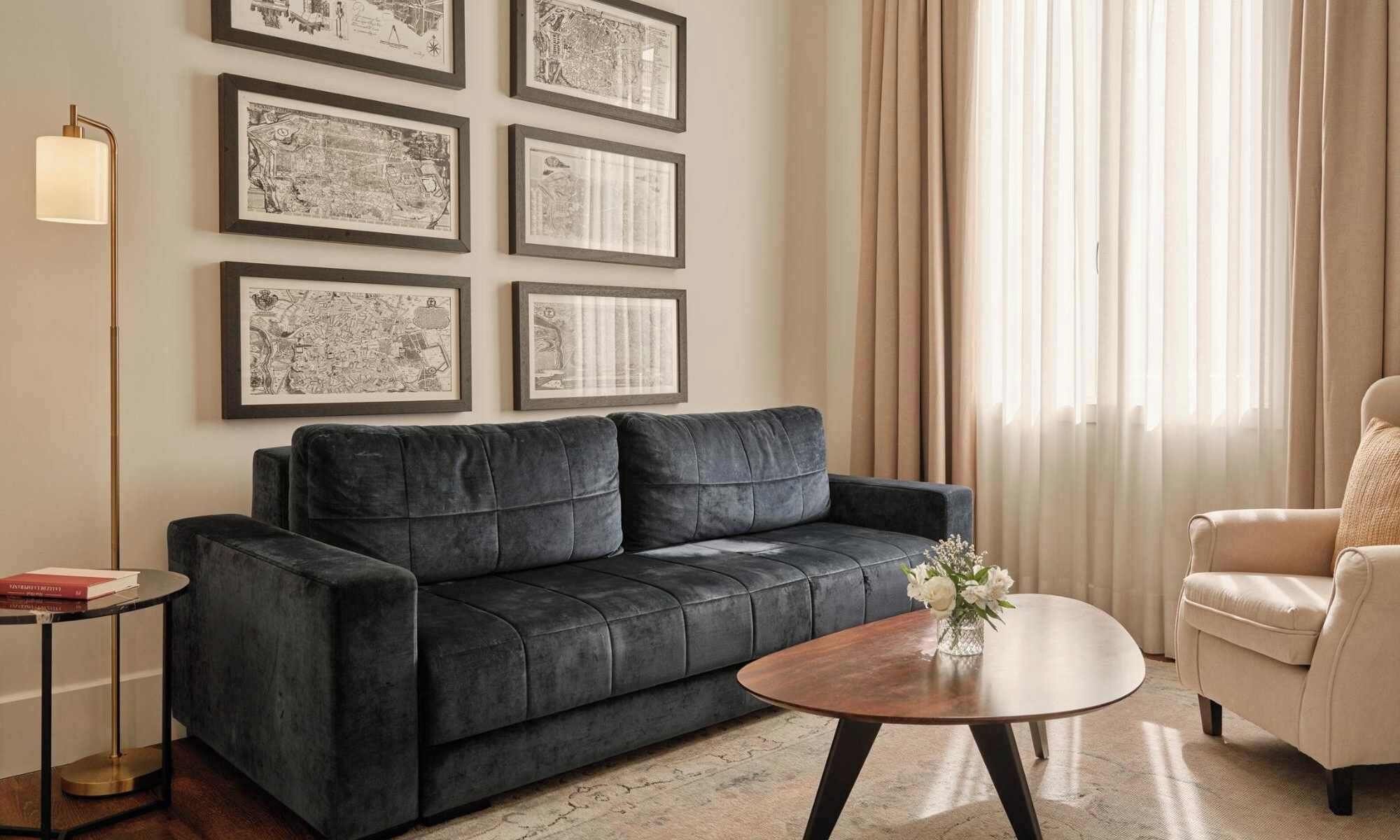 A living room with a dark sofa, a round coffee table, and a chair. There are framed pictures on the wall and a floor lamp.