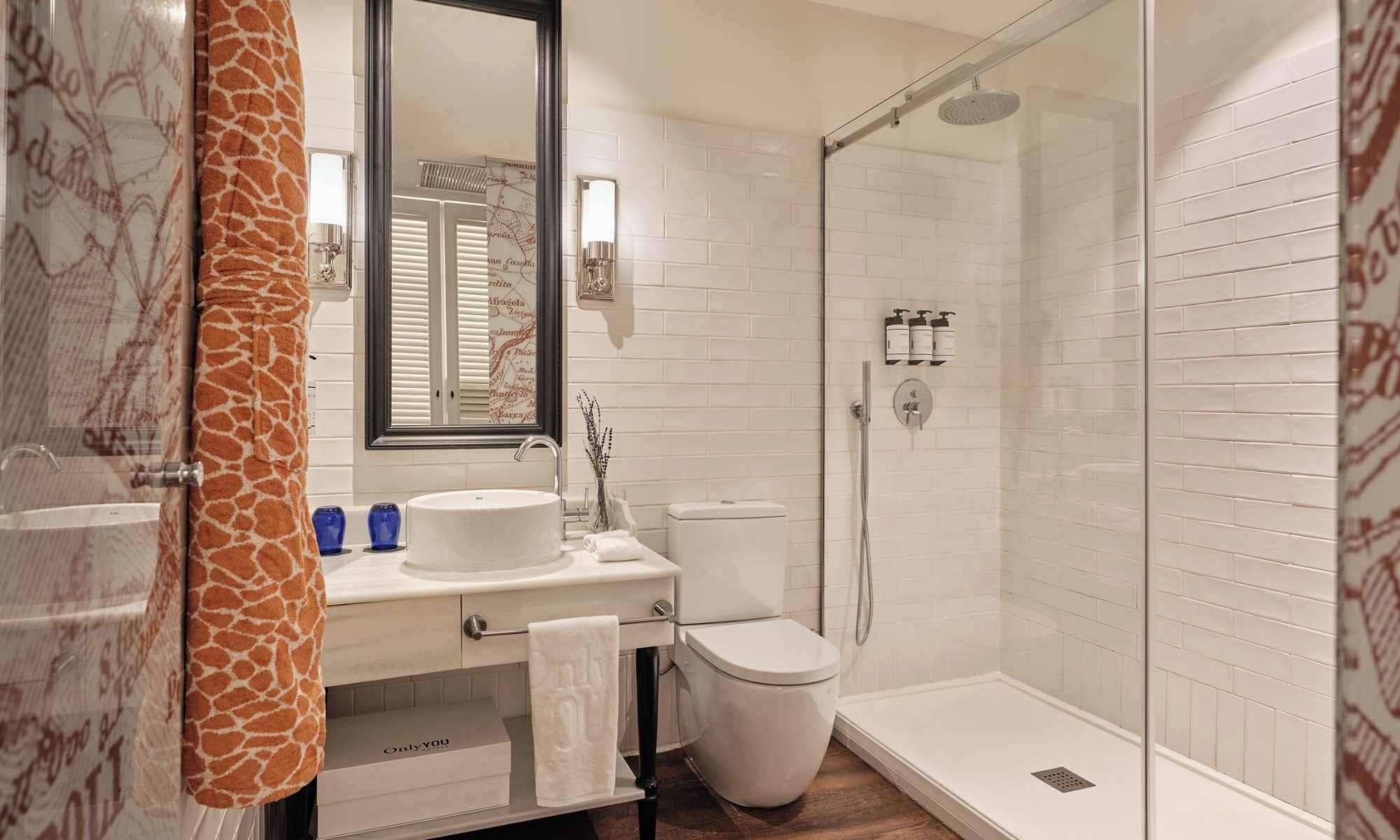 A modern bathroom with a white sink, mirror, and toilet, a shower with a glass door, and a giraffe-patterned towel.