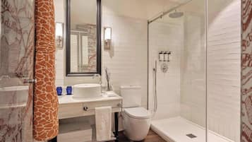 Un baño moderno con un lavabo, espejo y retrete blancos, una ducha con puerta de vidrio, y una toalla con estampado de jirafa.