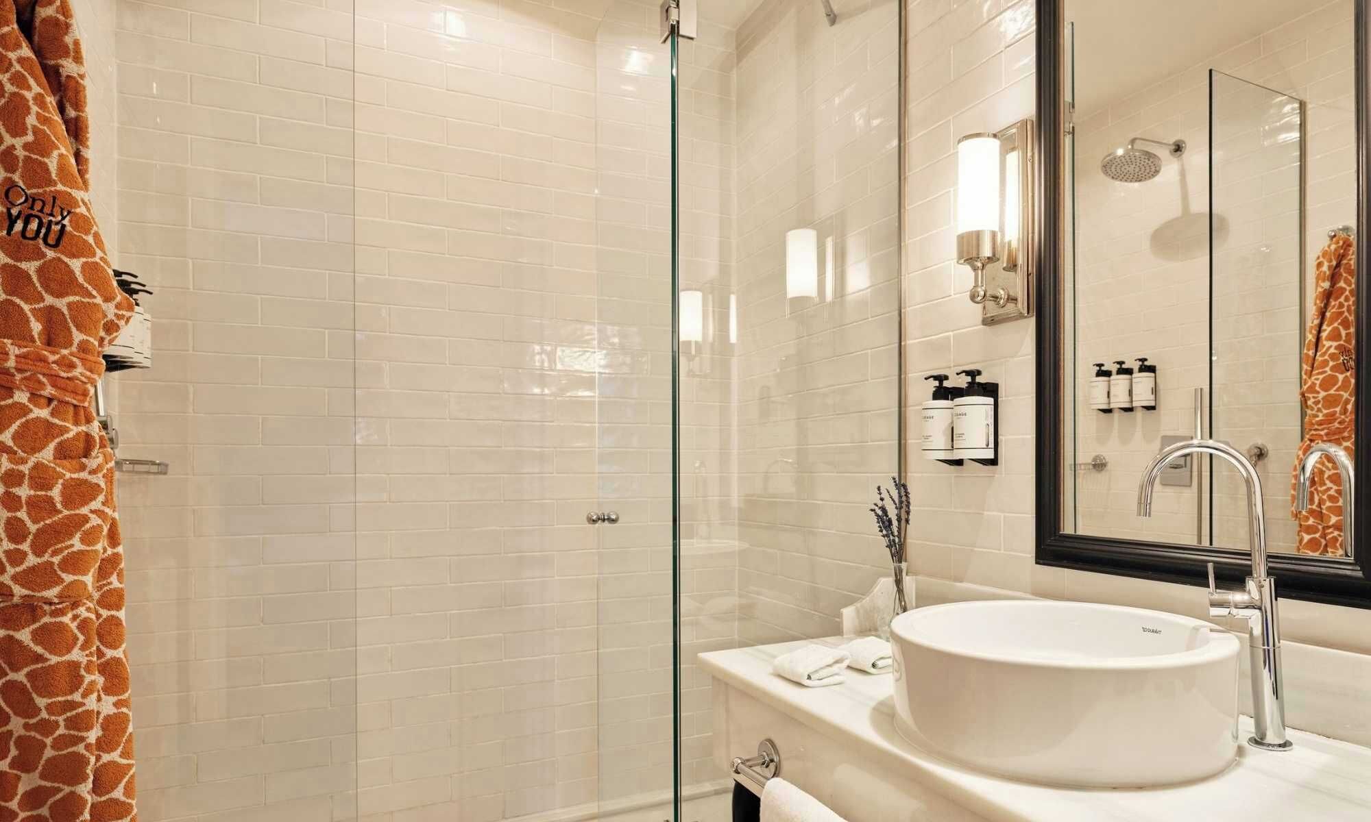 A modern bathroom with a glass shower enclosure, a white sink with a large mirror, and a giraffe-themed towel.