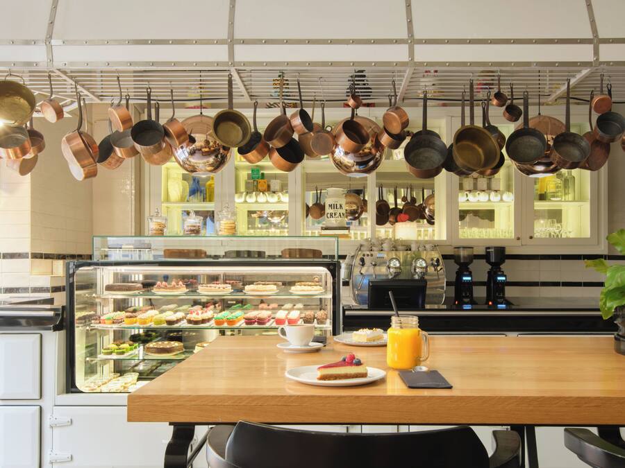 Una cafetería con una vitrina de pasteles, una máquina de café y ollas de cobre colgantes.