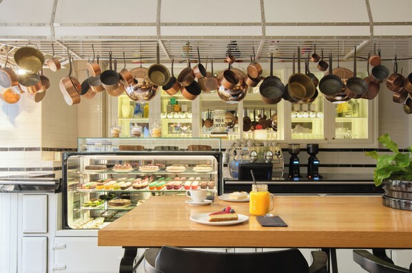 Un café avec une vitrine remplie de pâtisseries, une machine à café et des casseroles en cuivre suspendues au plafond.