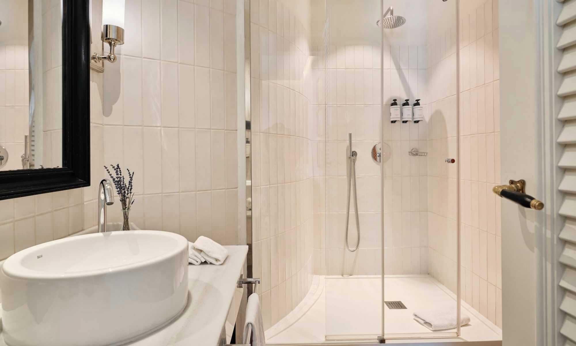 Une salle de bain avec un grand lavabo blanc, un miroir, une douche avec une porte en verre et un porte-serviettes.