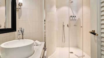 Une salle de bain avec un grand lavabo blanc, un miroir, une douche avec une porte en verre et un porte-serviettes.