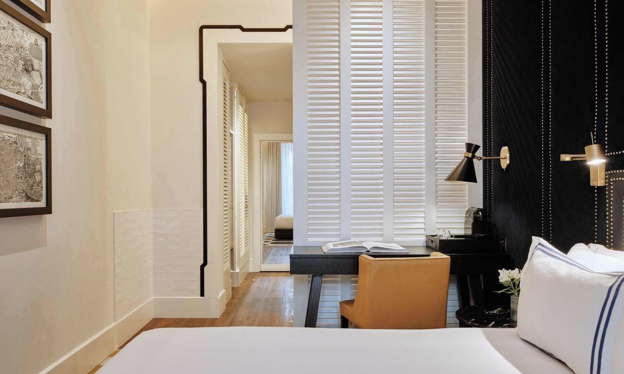 A hotel room with a bed, a desk, a chair, a coffee machine, and a black curtain.