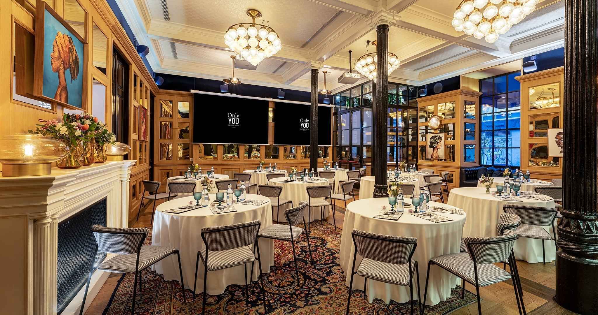 Un comedor formal con mesas redondas, sillas, candelabros y chimenea.