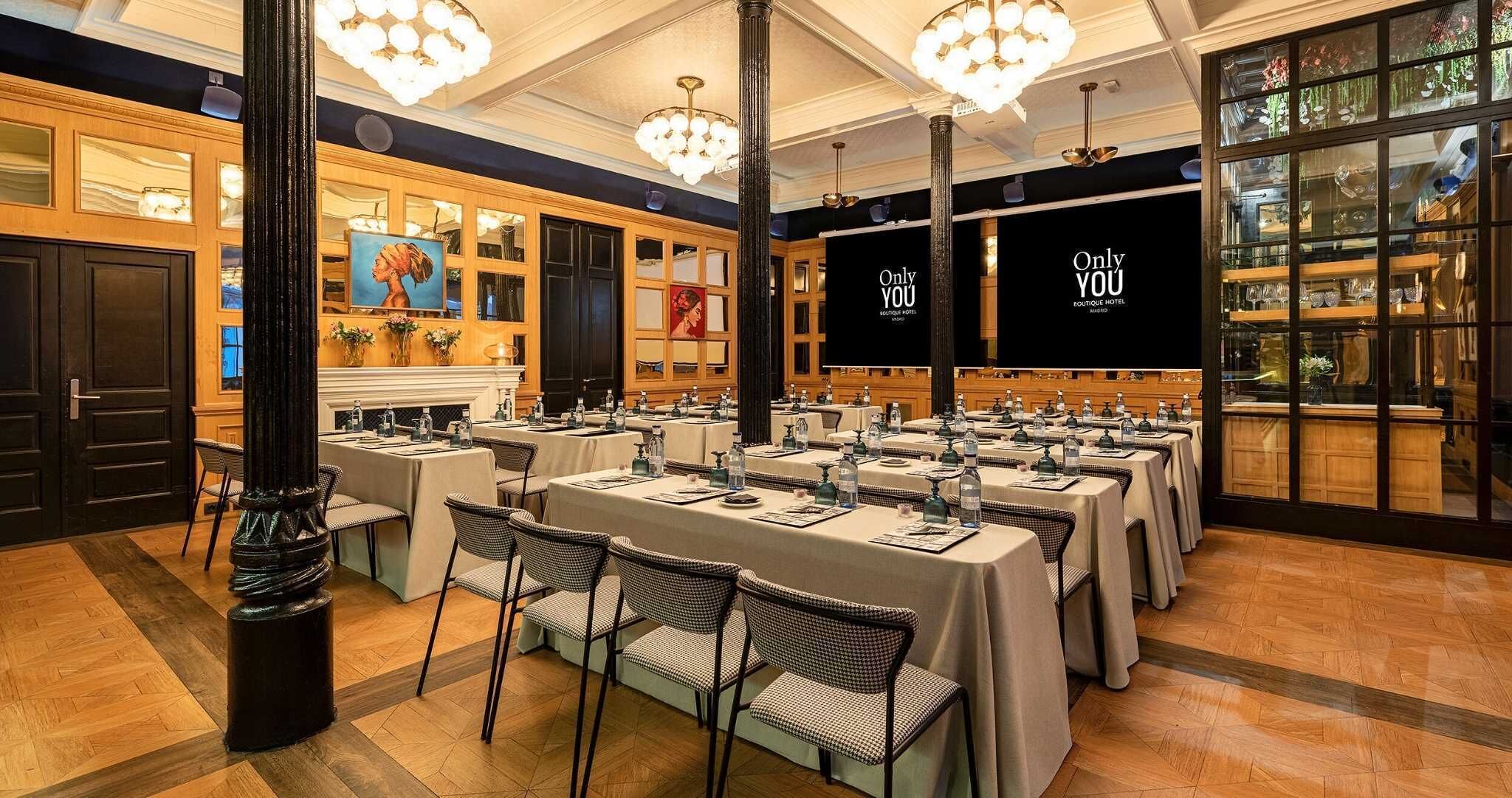 A conference room with tables set for a meeting, a large screen displaying 'Only YOU Boutique Hotel,' and a view of the hotel lobby through glass doors.