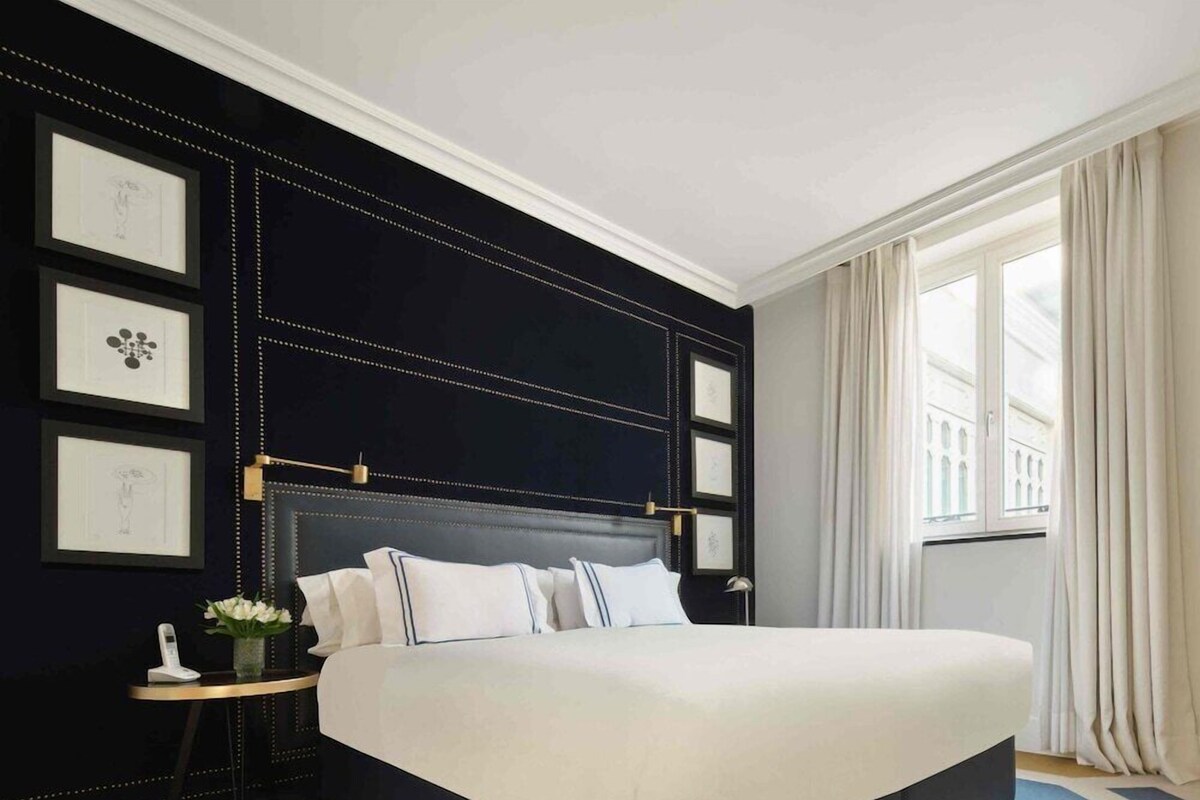 A modern hotel room with a large bed, a bedside table with a lamp, and framed artwork on the wall.