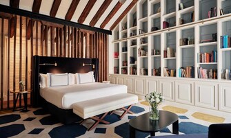 A bedroom with a large bed, a bookshelf, and a small table with a vase of flowers.