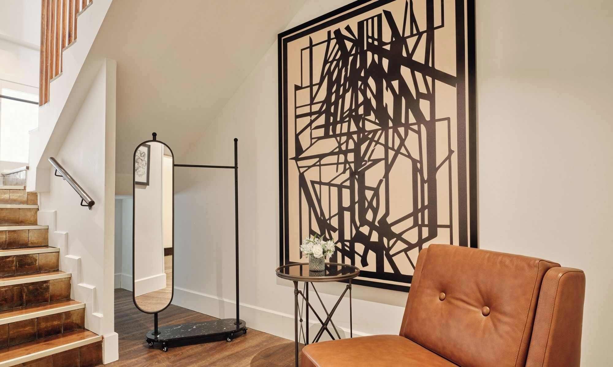 A staircase with a handrail, a wall-mounted mirror, a geometric art piece, and a brown leather chair.