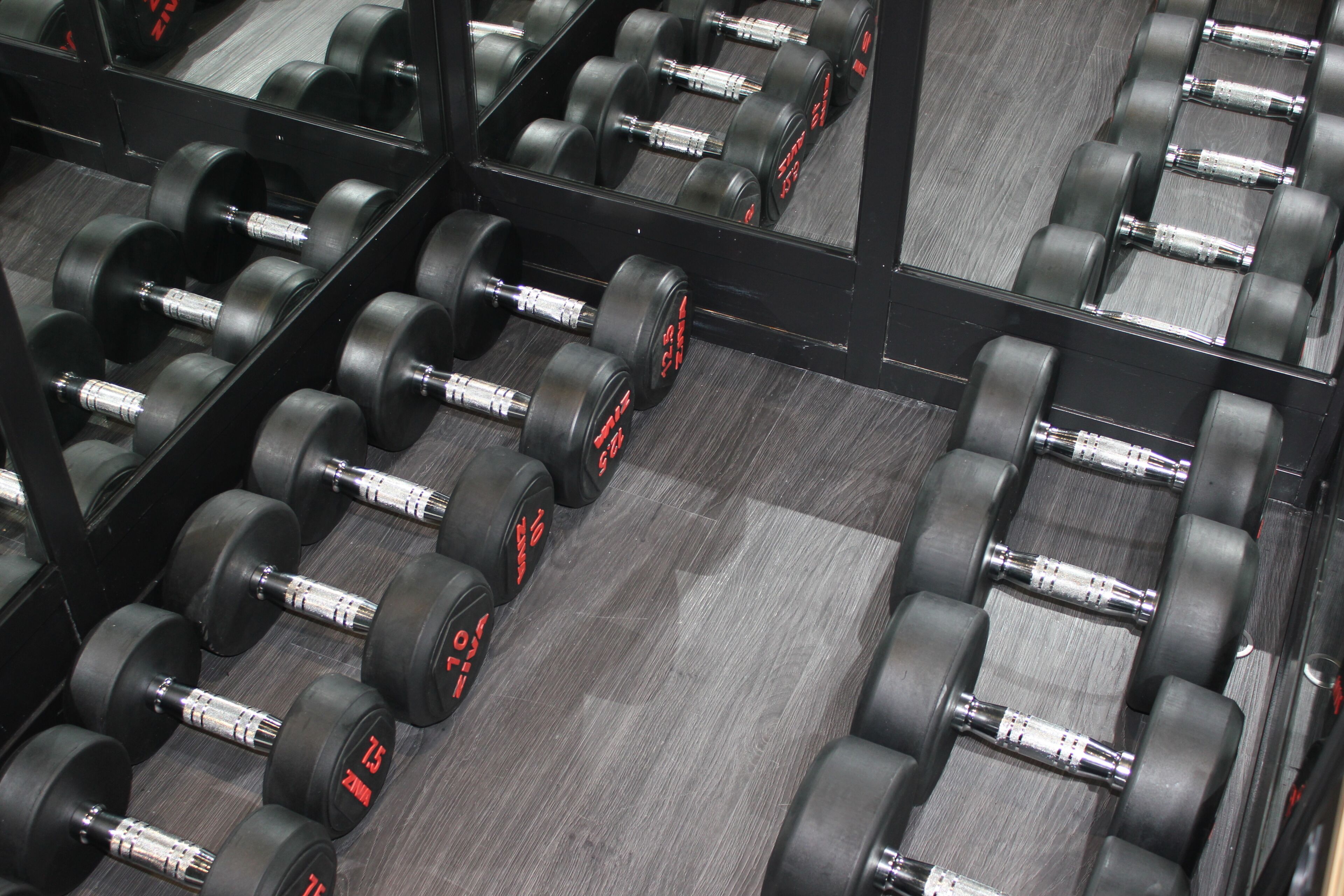 Un gimnasio con filas de mancuernas negras y paredes con espejos.