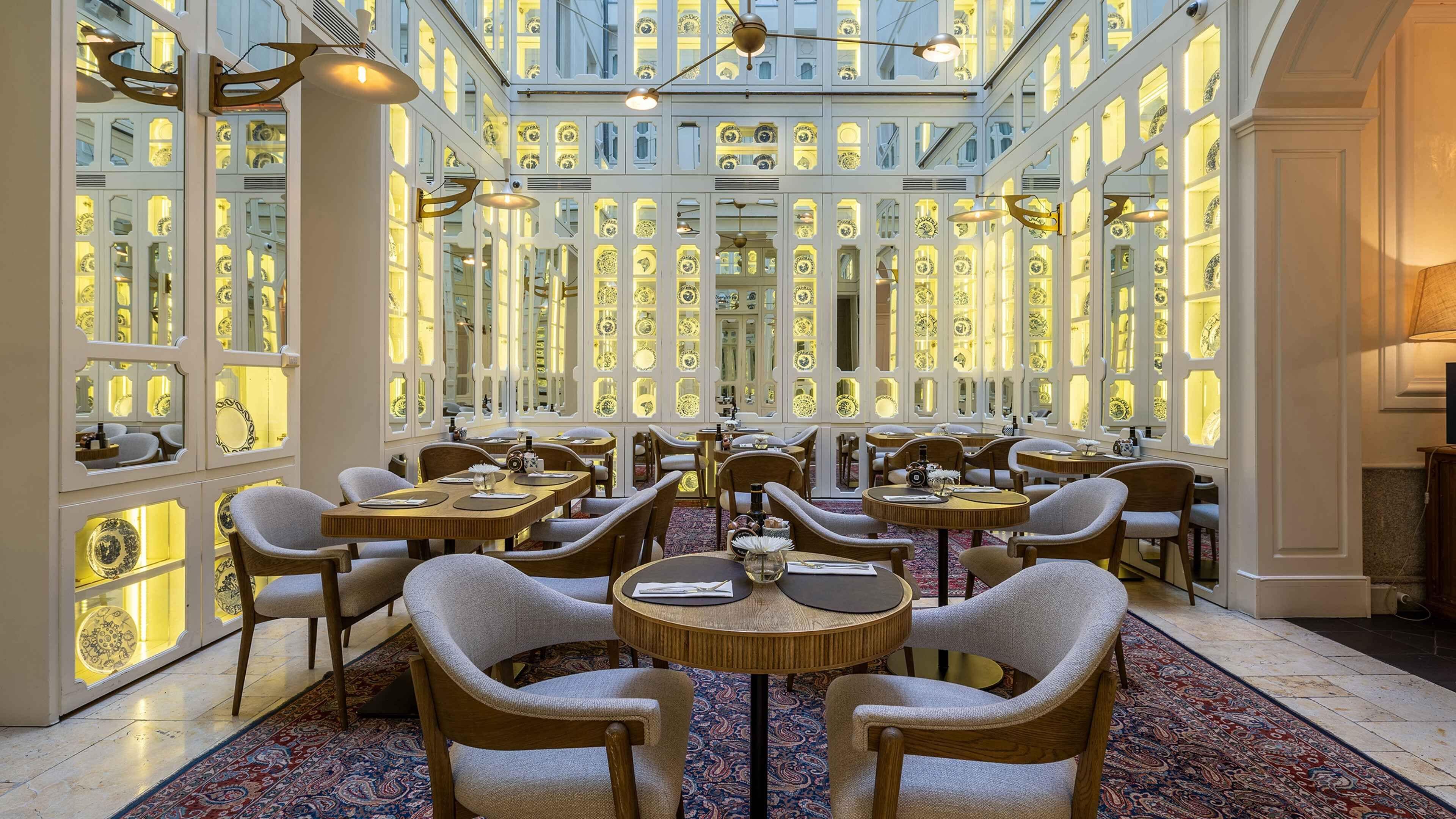 A spacious dining area with multiple tables and chairs, high ceilings, and decorative glass panels.
