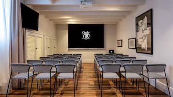 A conference room with rows of checkered chairs, a projector screen displaying 'Only YOU BOUTIQUE HOTEL Madrid', and framed artwork on the walls.