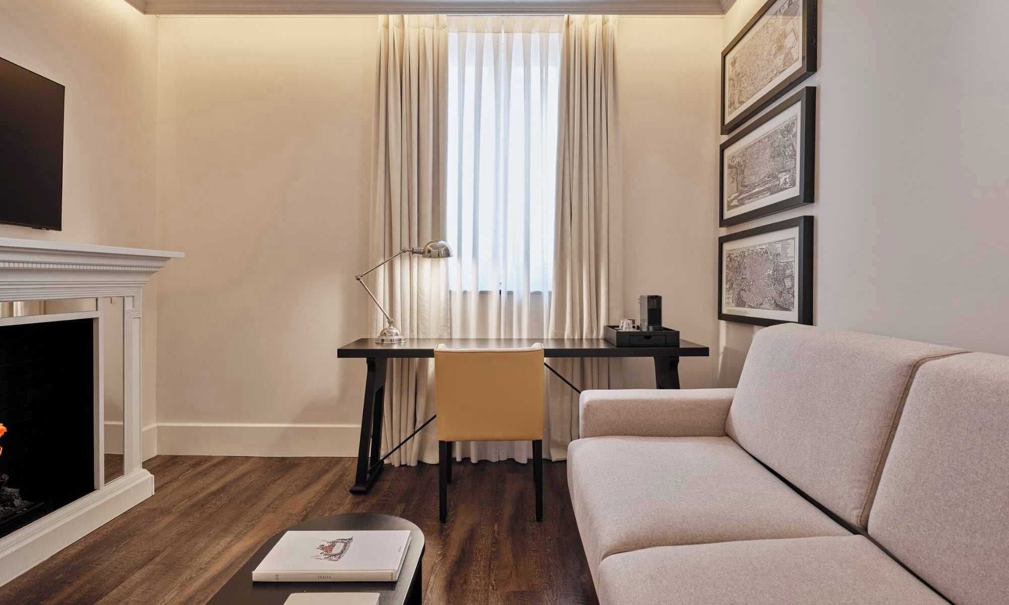 A living room with a fireplace, a sofa, a desk with a chair, and framed artwork on the wall.