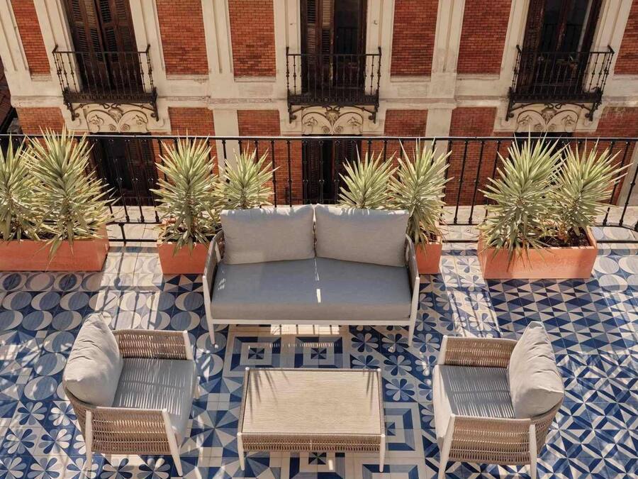 A balcony with a patterned floor, a gray sofa, wicker chairs, and potted plants.