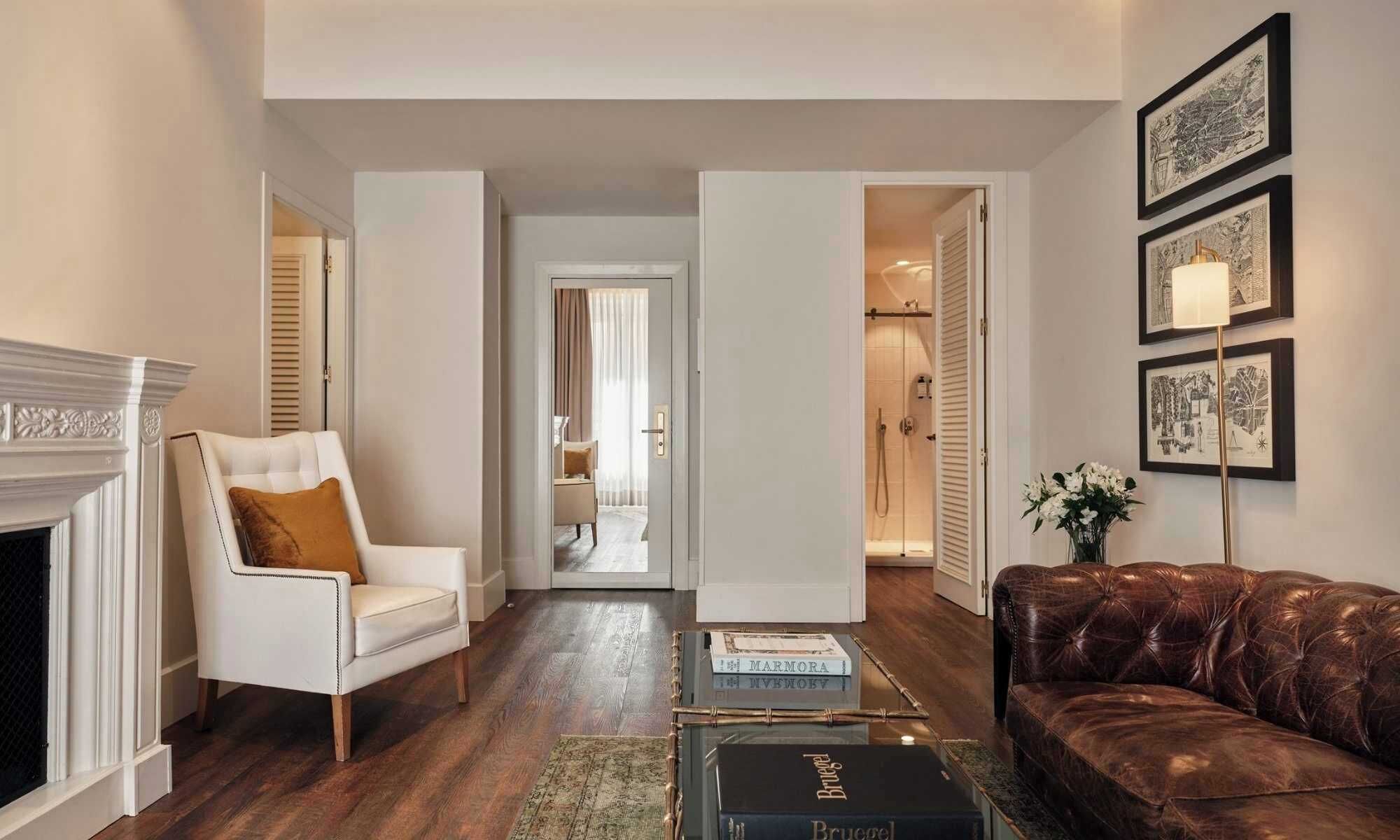 A living room with a fireplace, a leather couch, a coffee table with books, and a hallway leading to a bathroom.