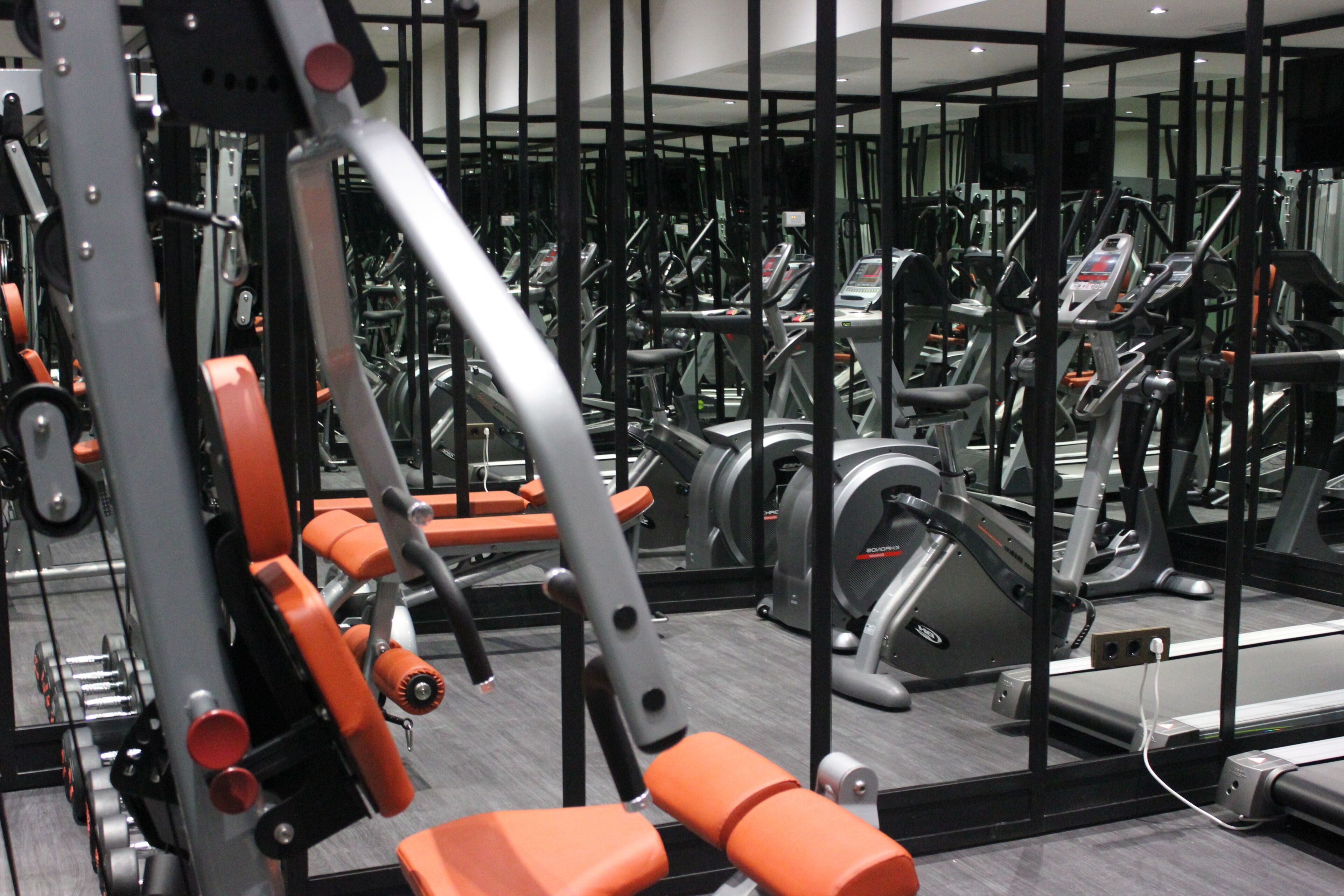 Un gimnasio con equipamiento de ejercicio y paredes espejadas.