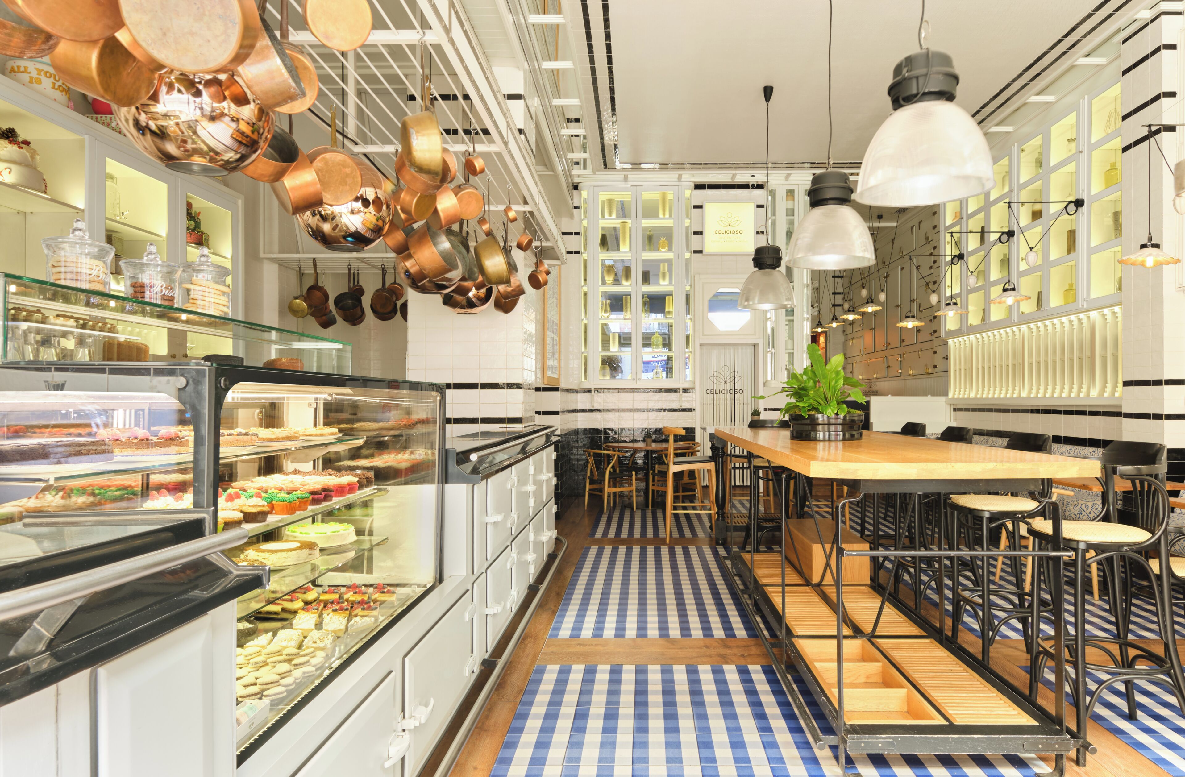 A modern kitchen with copper pots, a glass display case with food, and a blue and white checkered floor.