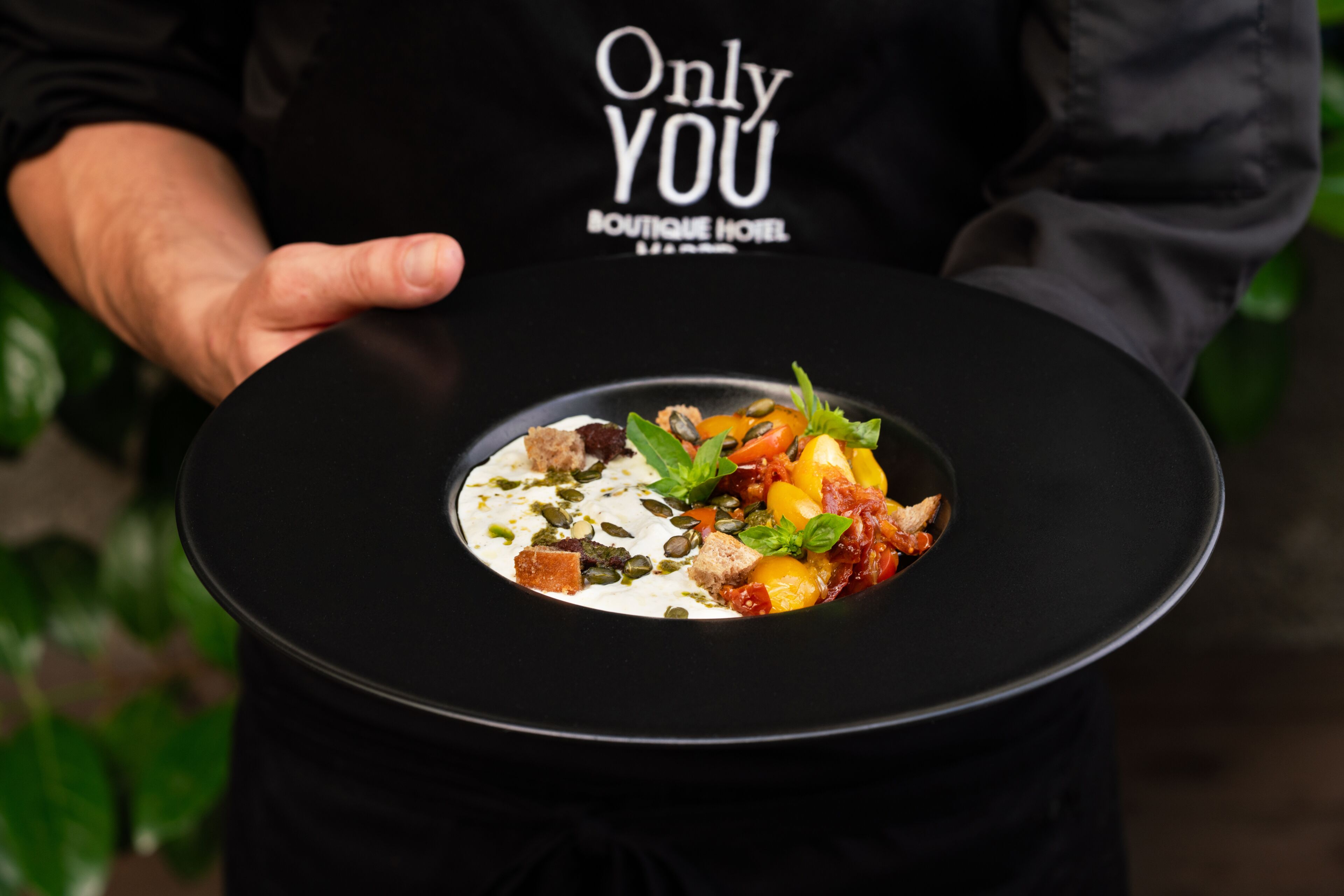 A person holding a black plate with a gourmet dish.