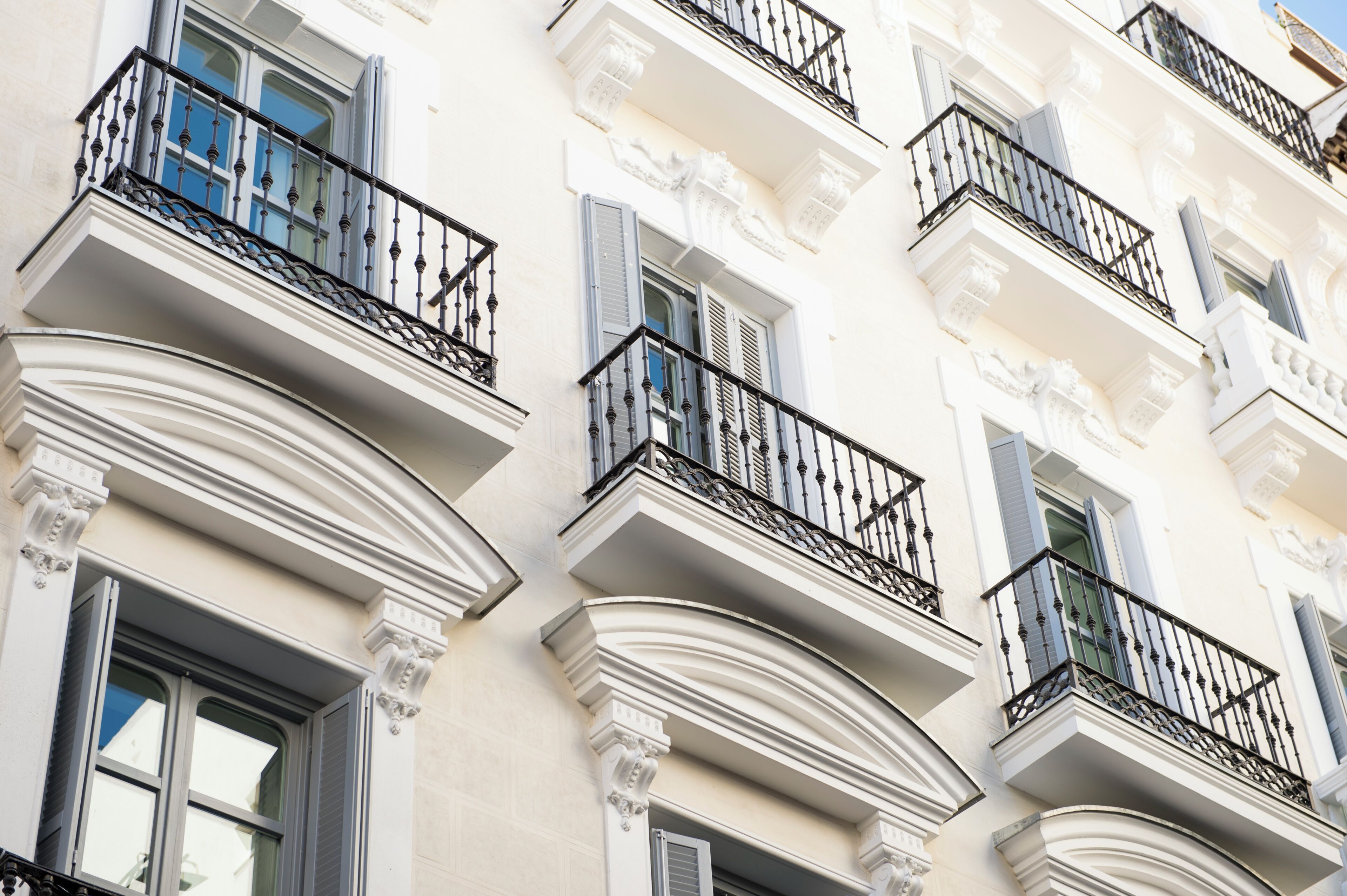 Un edificio de varios pisos con balcones, fachada blanca y detalles arquitectónicos clásicos.