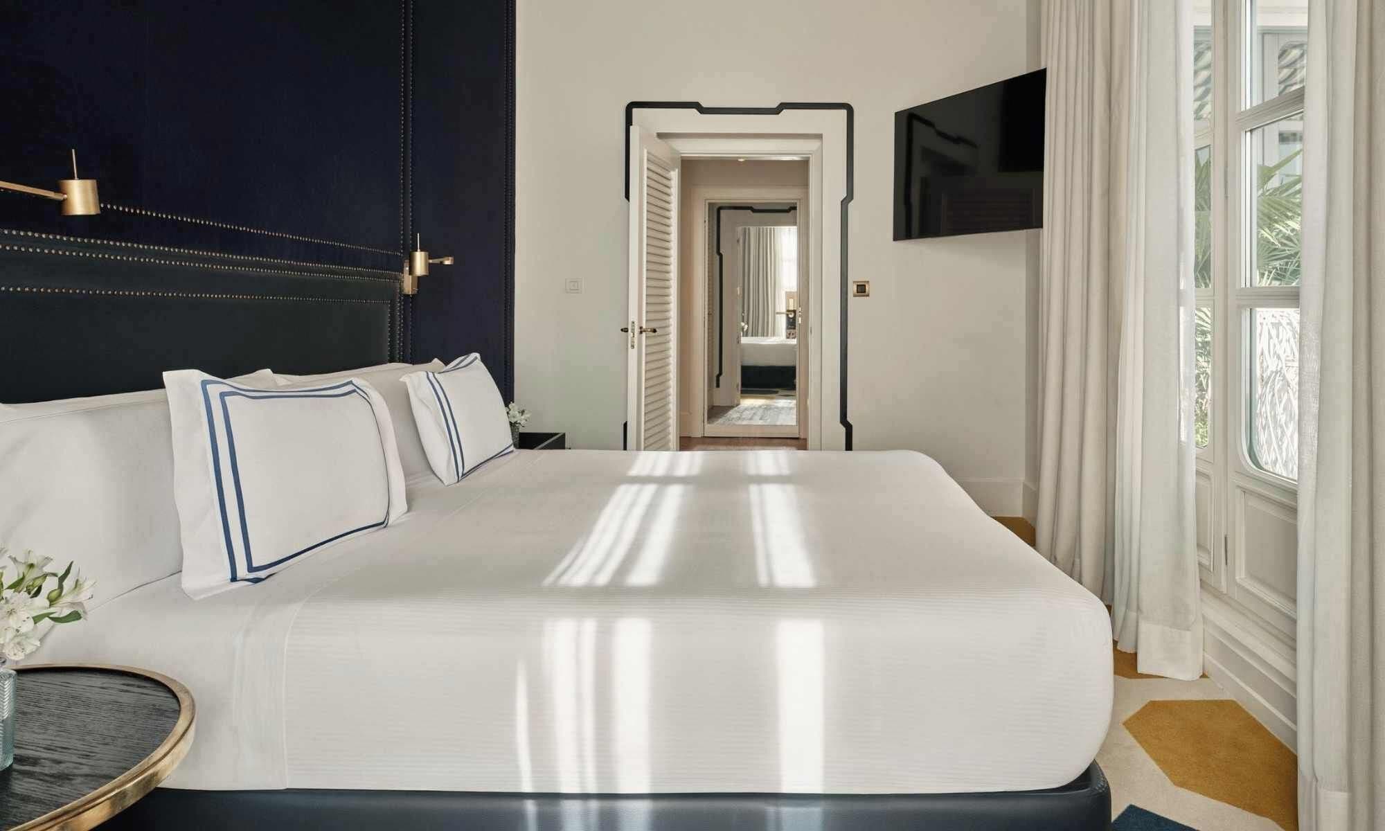 Une chambre d’hôtel avec un grand lit, une table de chevet, un téléviseur fixé au mur et donnant sur le couloir.