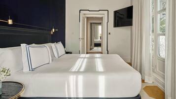 Une chambre d’hôtel avec un grand lit, une table de chevet, un téléviseur fixé au mur et donnant sur le couloir.