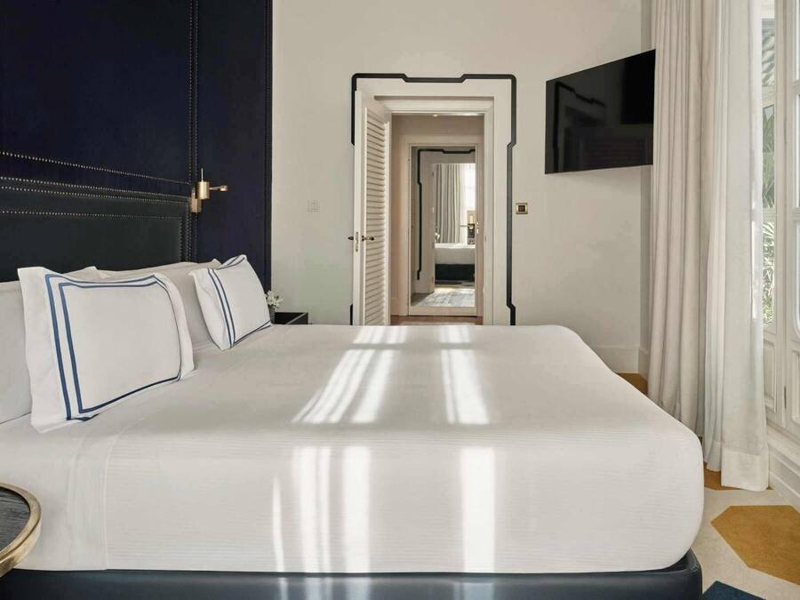 Habitación de hotel con una cama grande, una mesita de noche, televisor montado en la pared y vistas al pasillo.