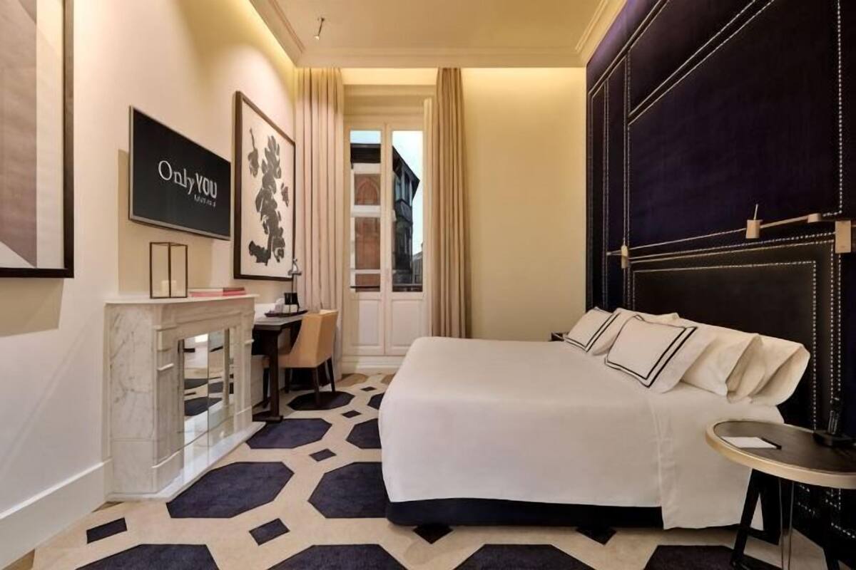 Une chambre d’hôtel avec un lit, un bureau, une chaise, une télévision et une fenêtre avec des rideaux.