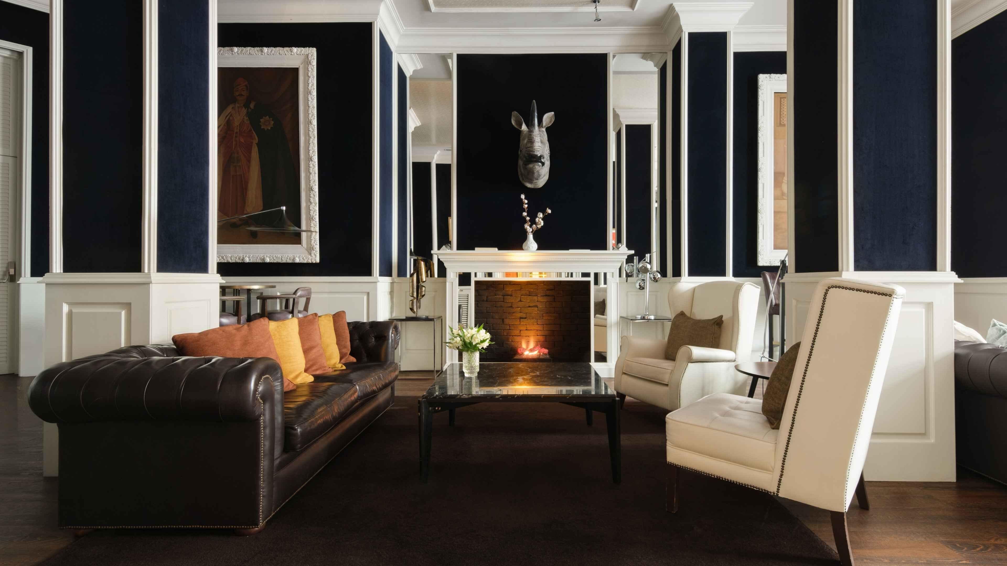 A living room with a fireplace, leather sofa, armchairs, and a decorative headpiece above the mantel.
