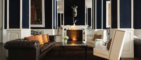 A living room with a fireplace, leather sofa, armchairs, and a decorative headpiece above the mantel.