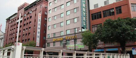 A multi-story hotel with a prominent Riverside Hotel sign, featuring a traditional architectural style with brickwork and multiple windows.