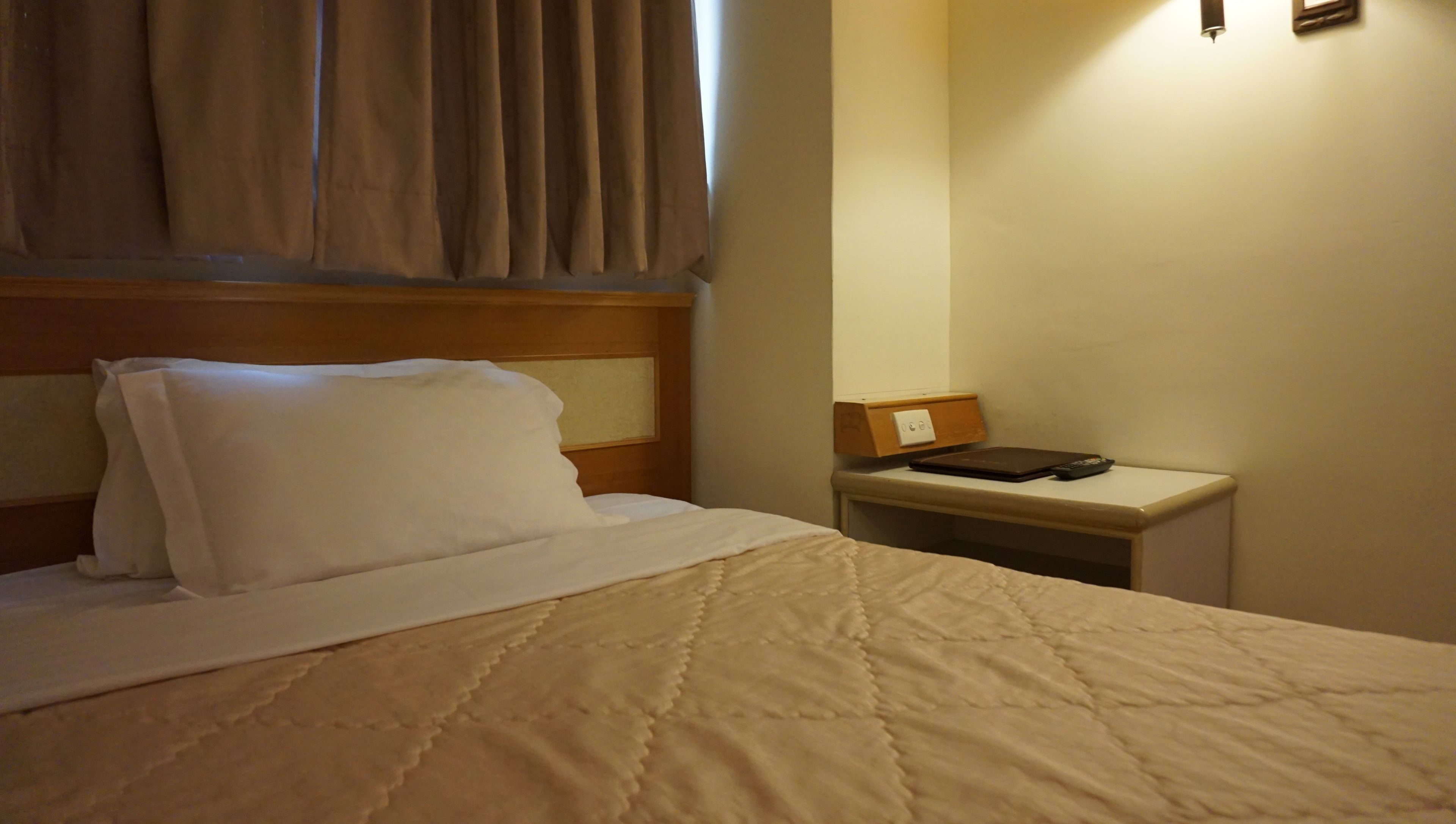 Une chambre d’hôtel avec un lit, une table de chevet, une lampe et une fenêtre avec des rideaux.