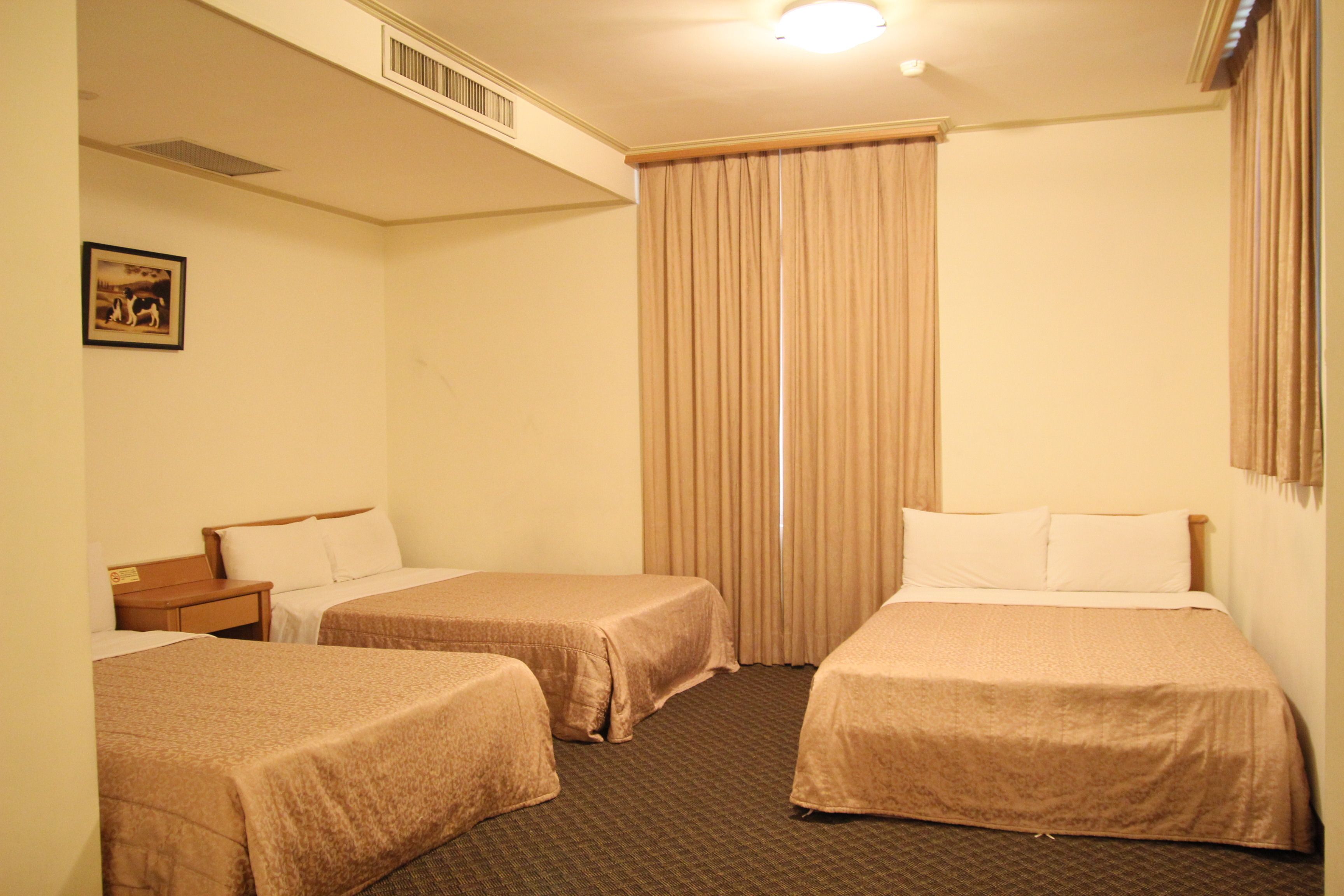 A hotel room with two single beds, a wooden nightstand, a small table, and a picture on the wall.