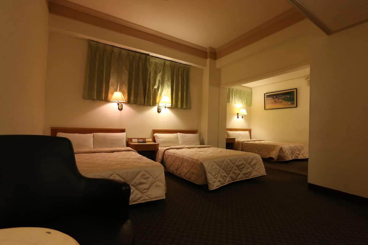 Ein Hotelzimmer mit drei Betten, einem Sessel und einem Gemälde an der Wand.
