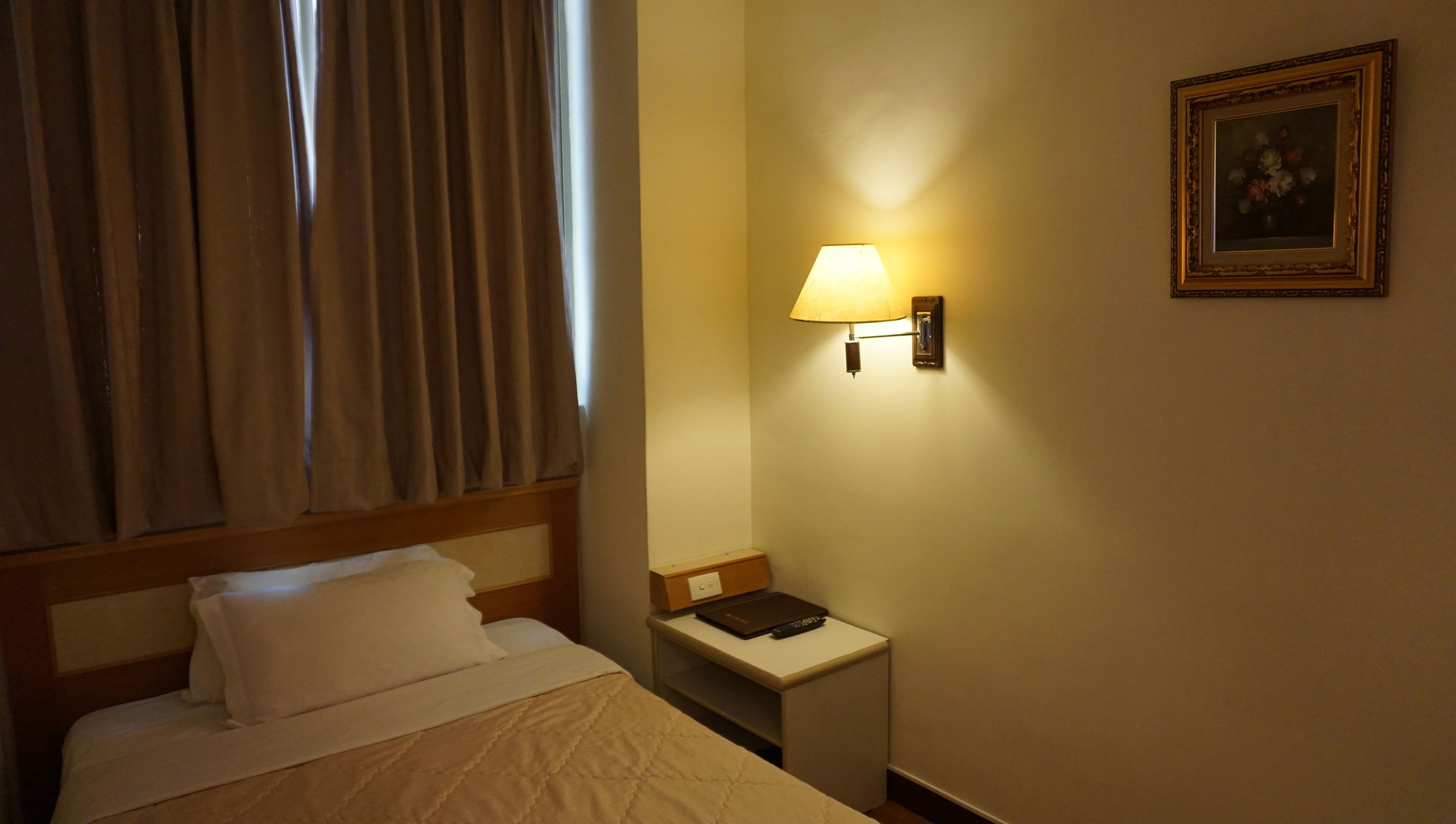 A hotel room with a bed, a nightstand with a lamp, and a framed picture on the wall.