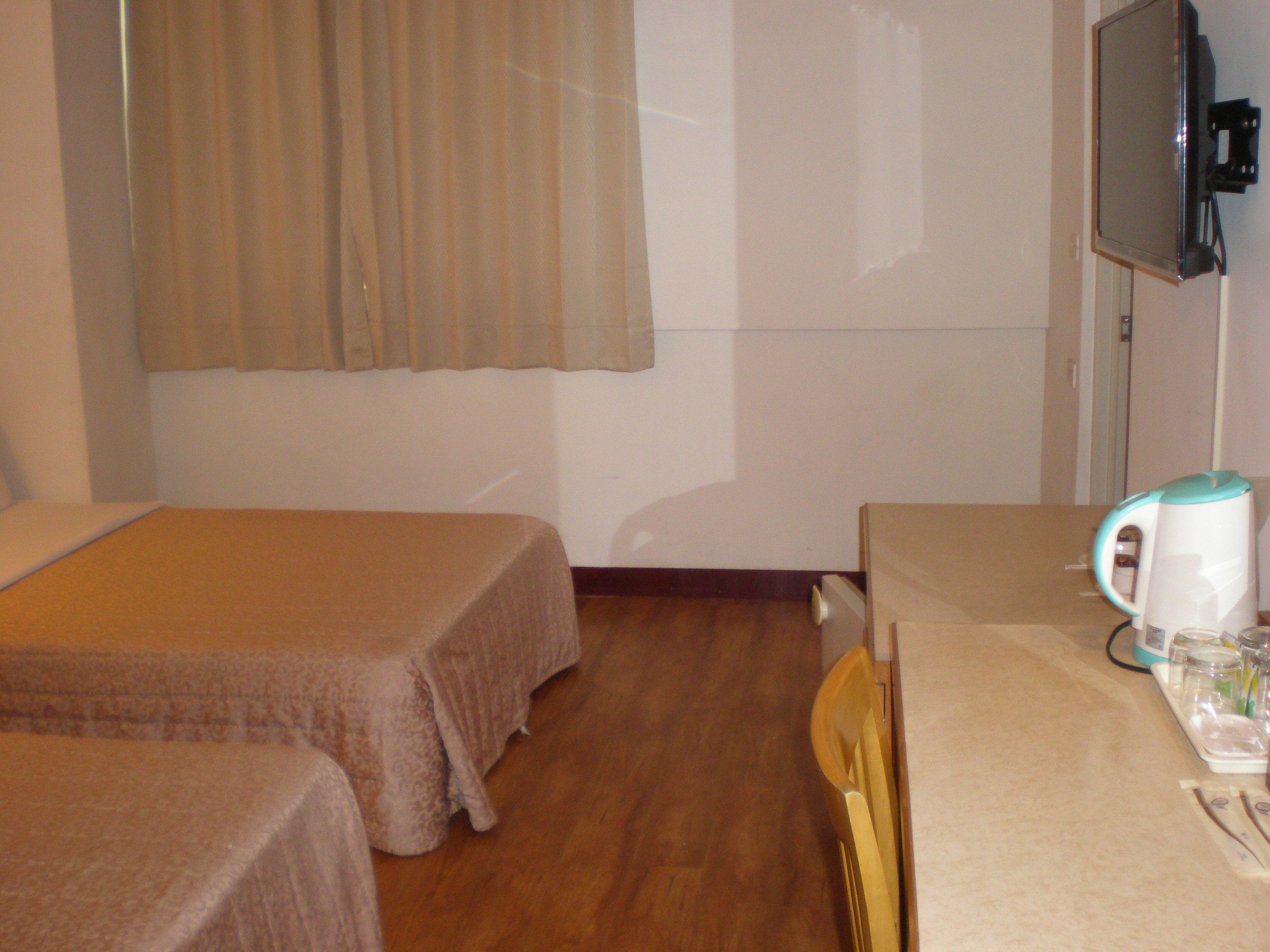 A hotel room with two single beds, a wooden floor, a small table with a kettle, glasses, and a tray.