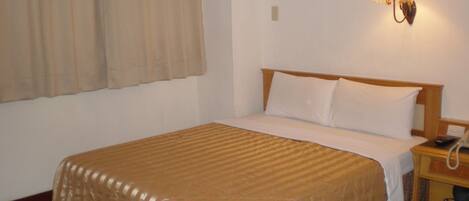 Habitación de hotel con cama, mesita de noche con teléfono y pantuflas, y lámpara de pared.