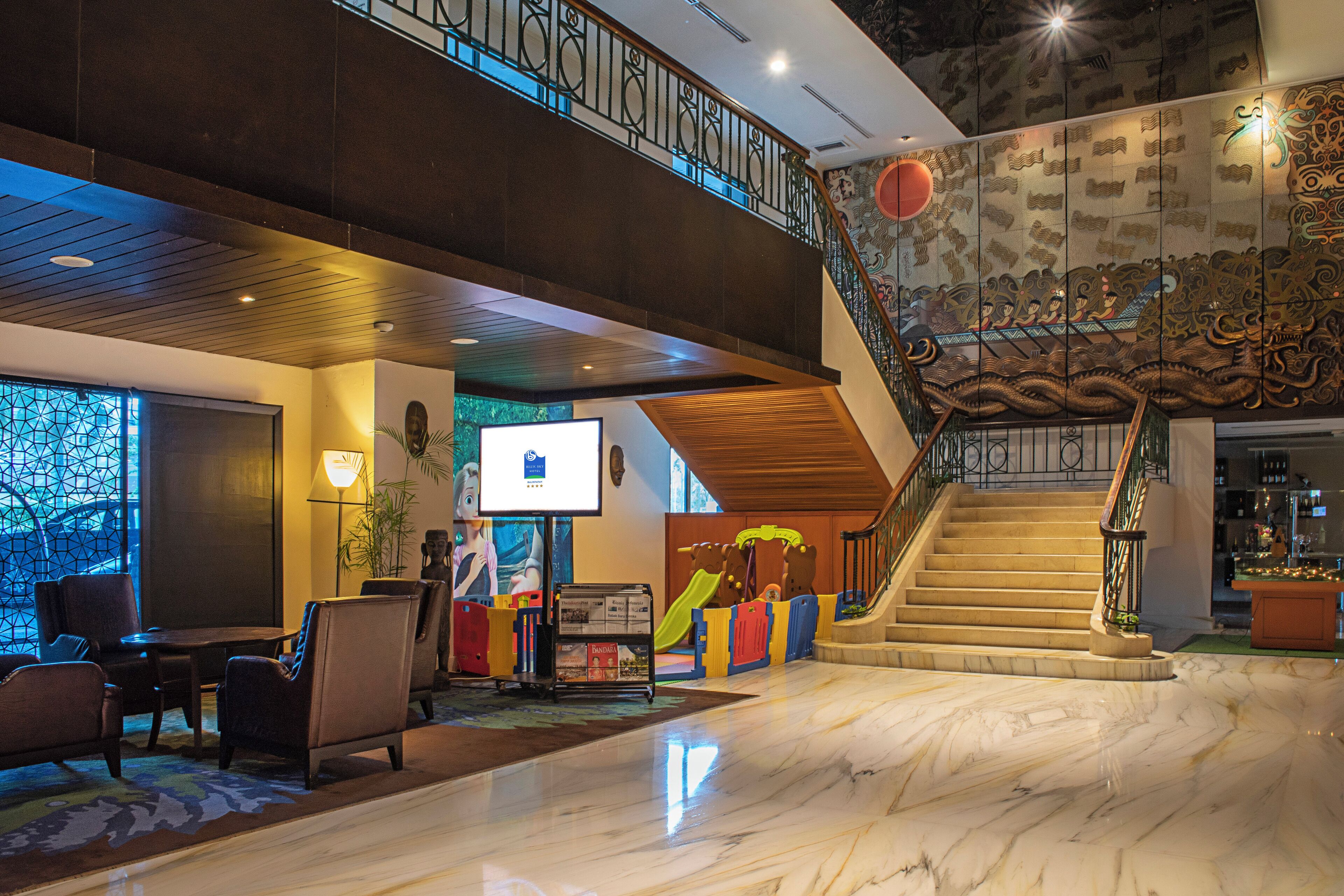 A lobby with a marble floor, a staircase with ornate railings, and a play area for children.