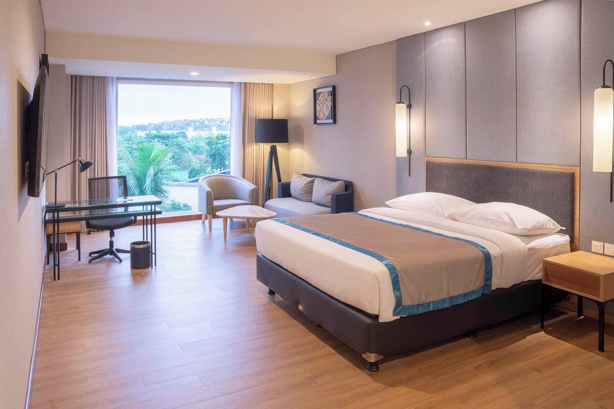 Habitación de hotel con una cama grande, un escritorio con silla, una mesita pequeña y un televisor montado en la pared.