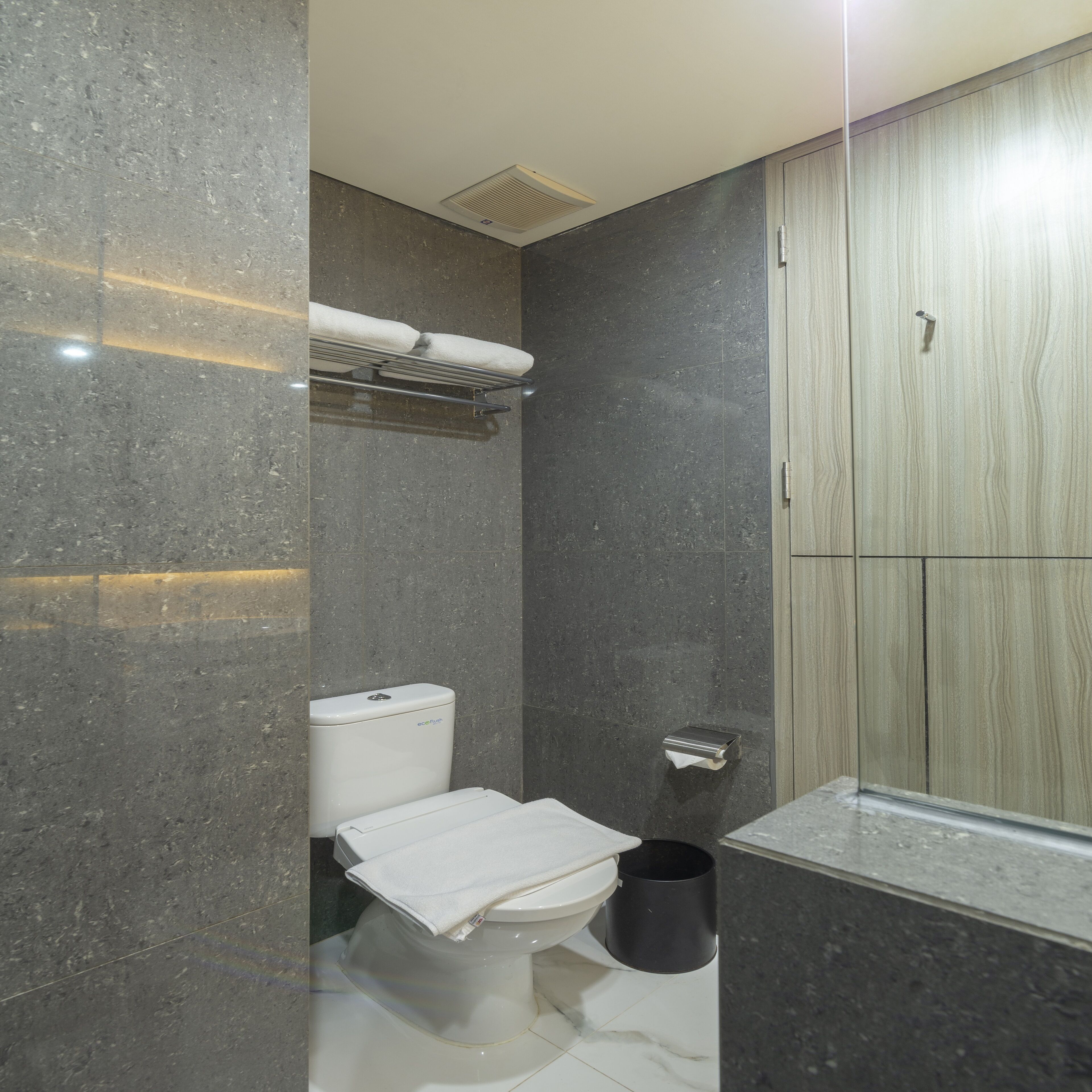 A modern bathroom with a toilet, a towel rack, a paper towel dispenser, and a shower area.