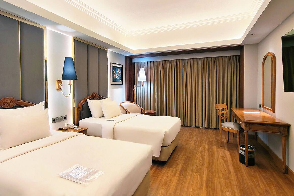 Habitación de hotel con dos camas, un escritorio, una silla, una lámpara, un teléfono y un cuadro en la pared.