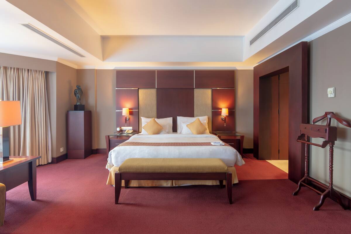 Una habitación de hotel con una cama grande, dos mesitas de noche, un banco, un escritorio y un armario.