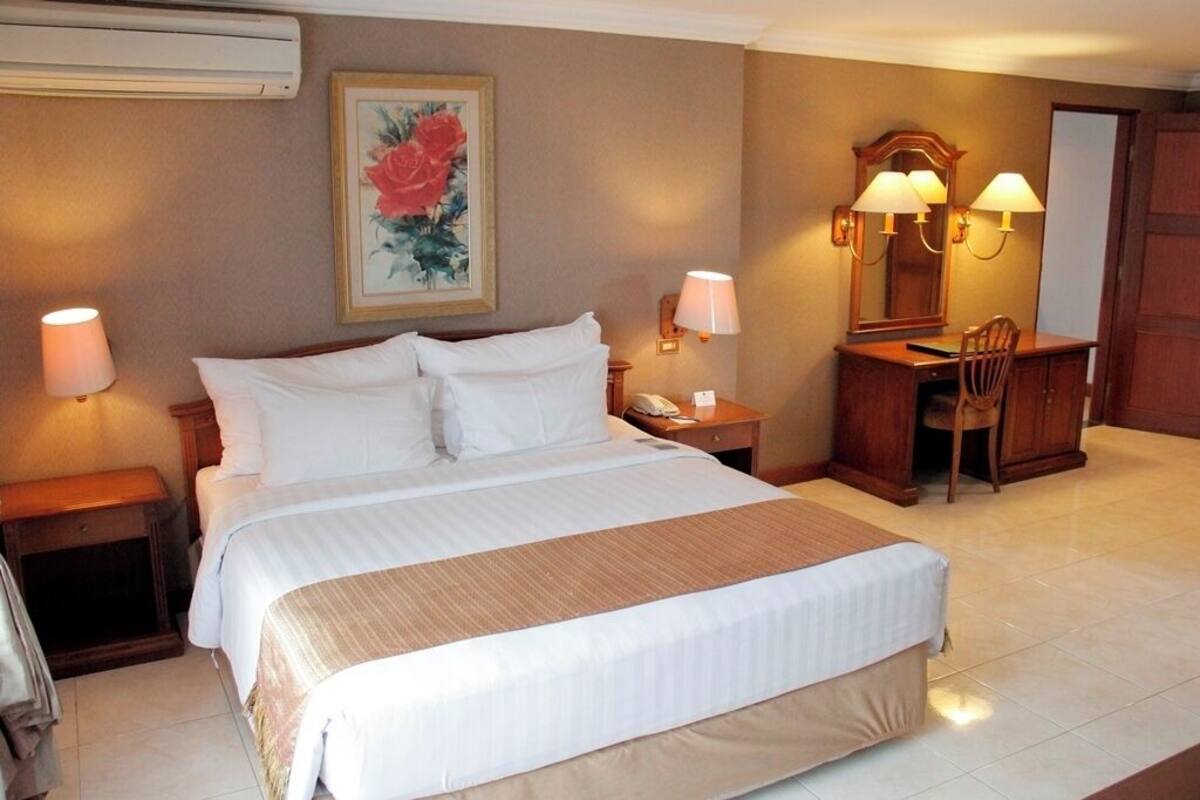 Habitación de hotel con una cama grande, un escritorio con silla, un espejo y dos lámparas de noche.