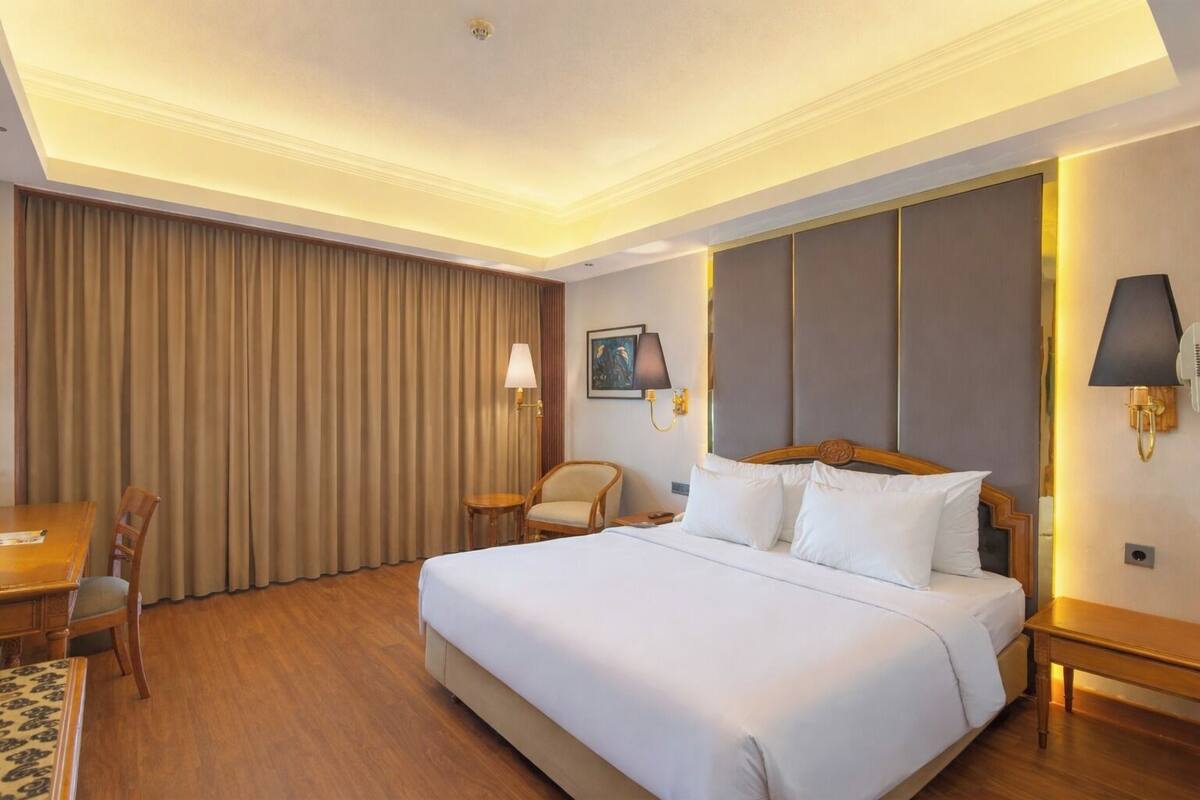 Una habitación de hotel con una cama grande, un escritorio, una silla, una lámpara y un cuadro en la pared.