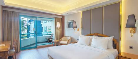 Hotelkamer met een groot bed, een bureau, een stoel, een klein tafeltje en een balkon met uitzicht op gebouwen.
