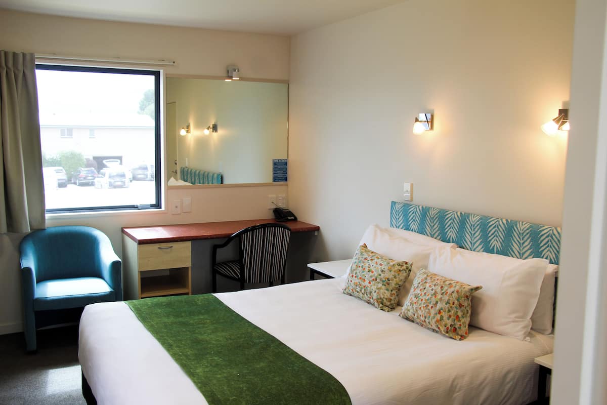 A hotel room with a bed, a desk, a chair, a large window, and a mirror.