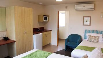 A hotel room with two beds, a desk, a microwave, a chair, and an air conditioning unit.
