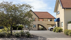 A two-story building with a red-tiled roof, a covered driveway, and a parking area. - Bella Vista Motel Mosgiel (Mosgiel)