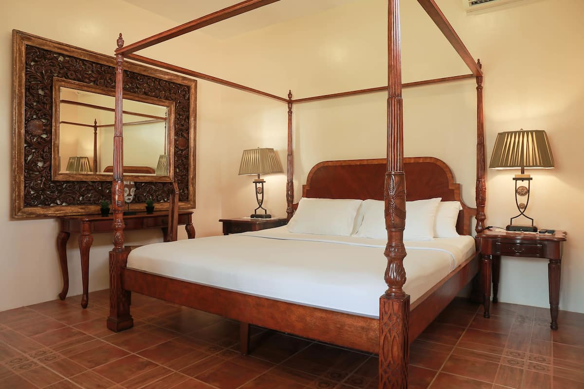 A four-poster bed with a wooden frame and white bedding, flanked by two nightstands with lamps, and a large ornate mirror on the wall.