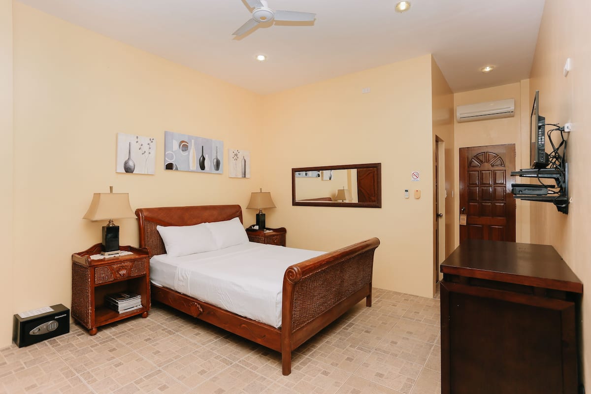 A hotel room with a wooden bed, two bedside tables, a ceiling fan, and wall-mounted artwork.